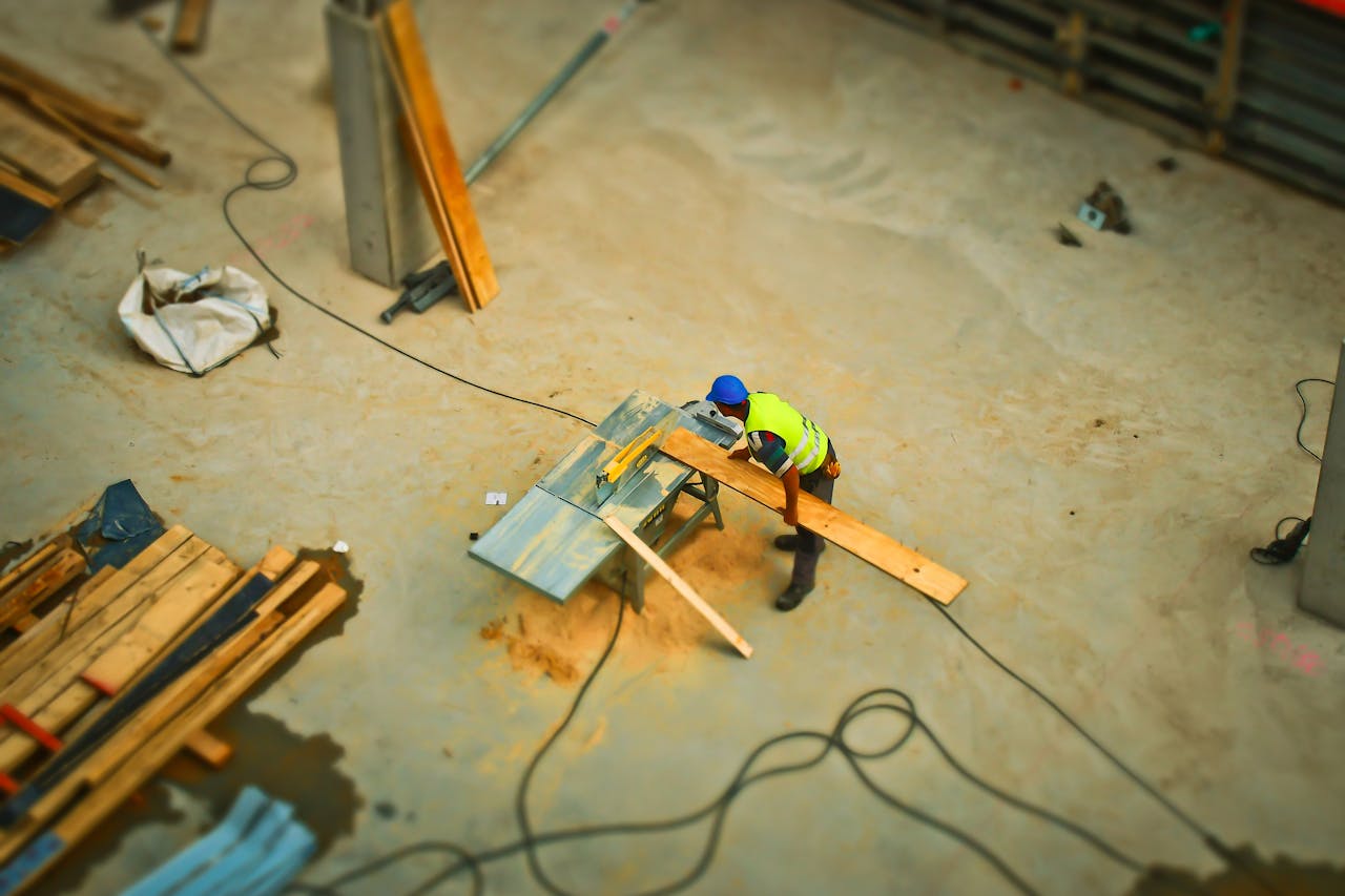 why-choose-us-img Overhead view of a construction worker using a saw to cut wood at a construction site.